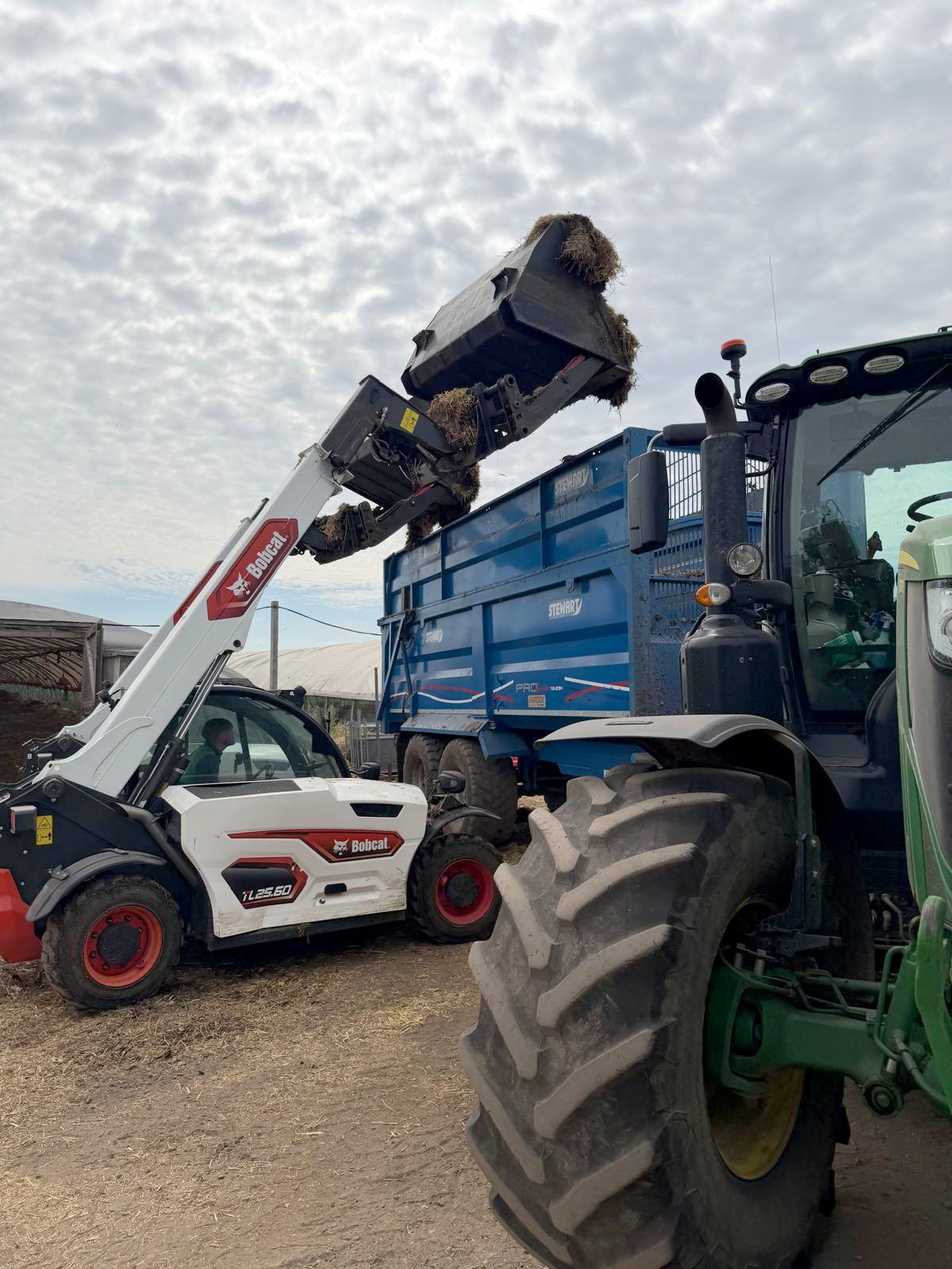 Bobcat telehandler loading litter into a trailer behind a tractor