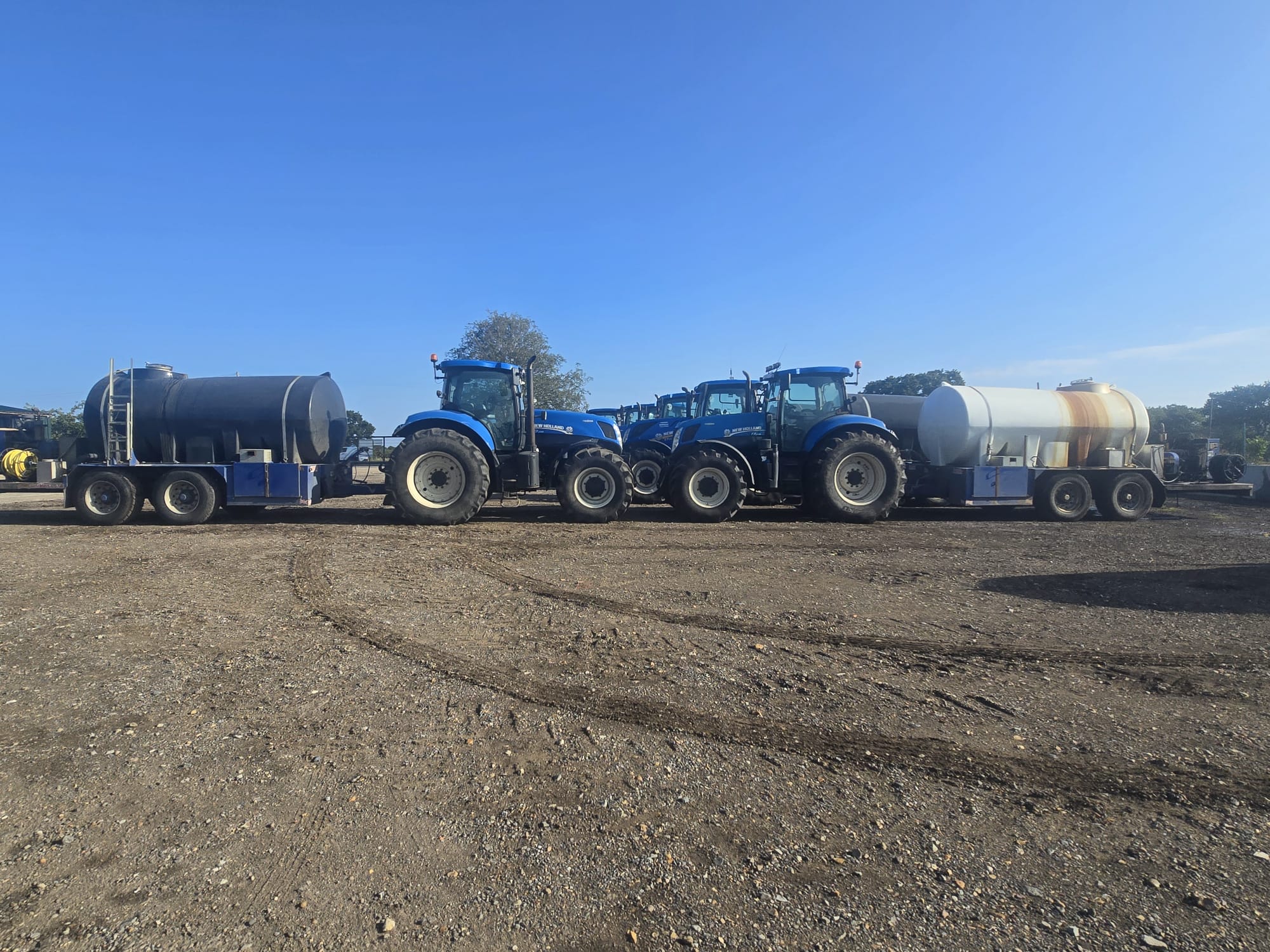 New Holland tractors each hitched to a water bowser in the yard