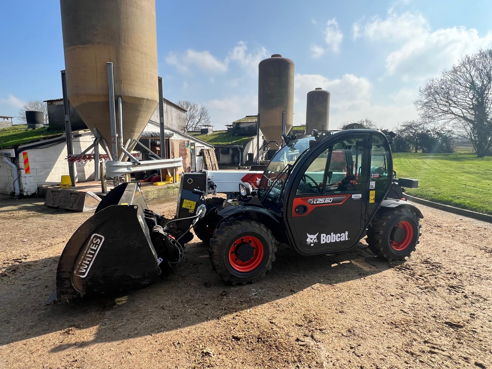 Bobcat telehandler with bucket parked by feed silos on a farm