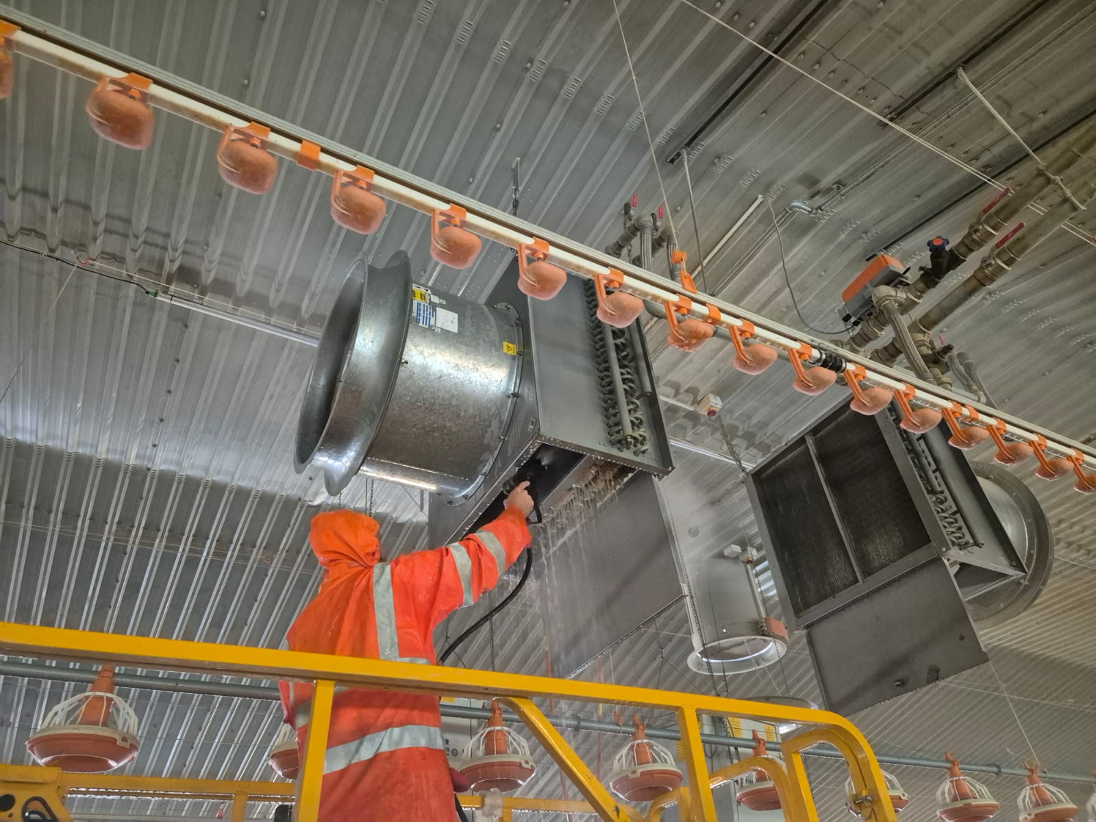 Close-up of a pressure washer cleaning fans and heaters at ceiling level