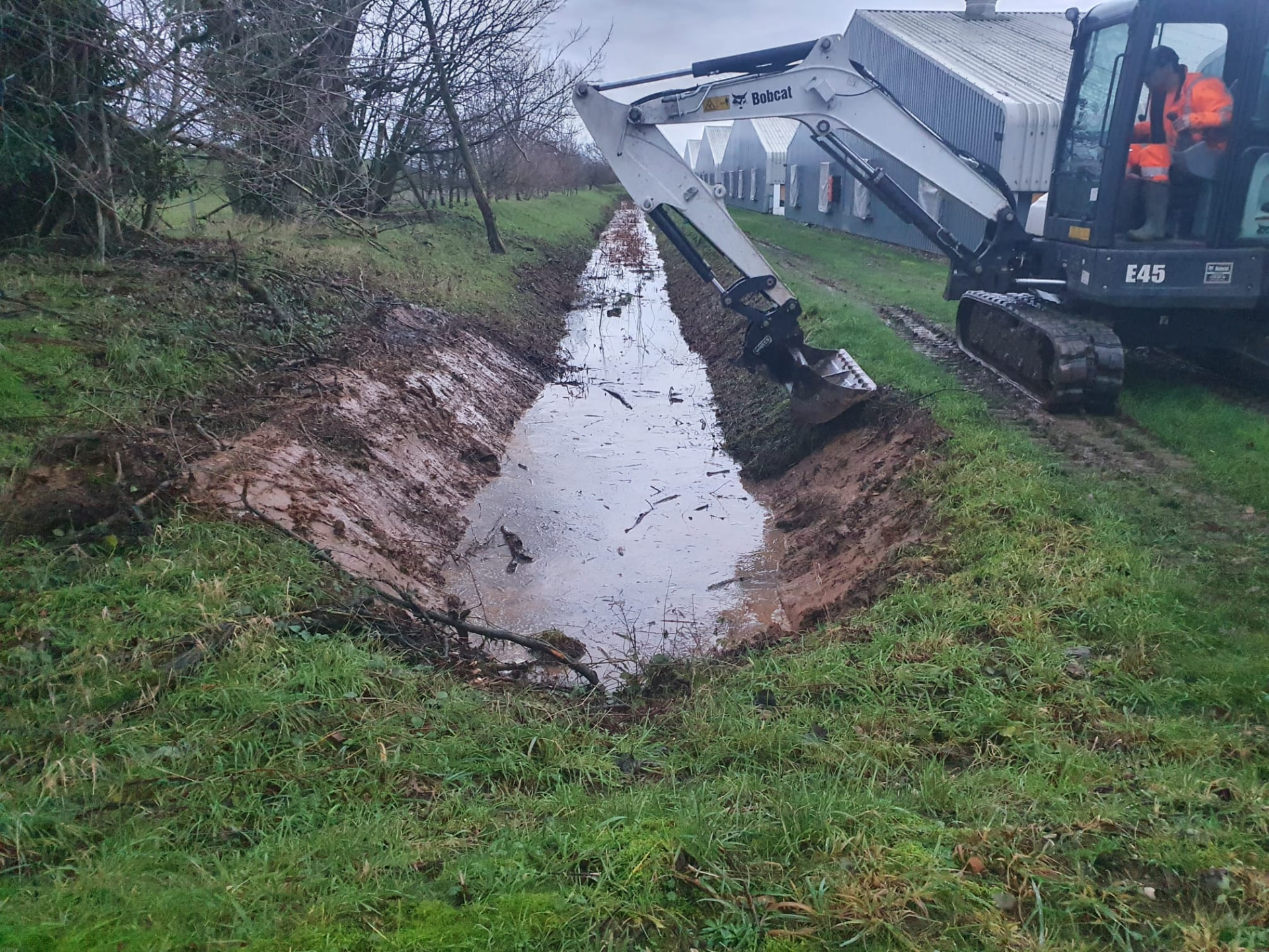 Bobcat E45 excavator digging out a ditch alongside poultry sheds