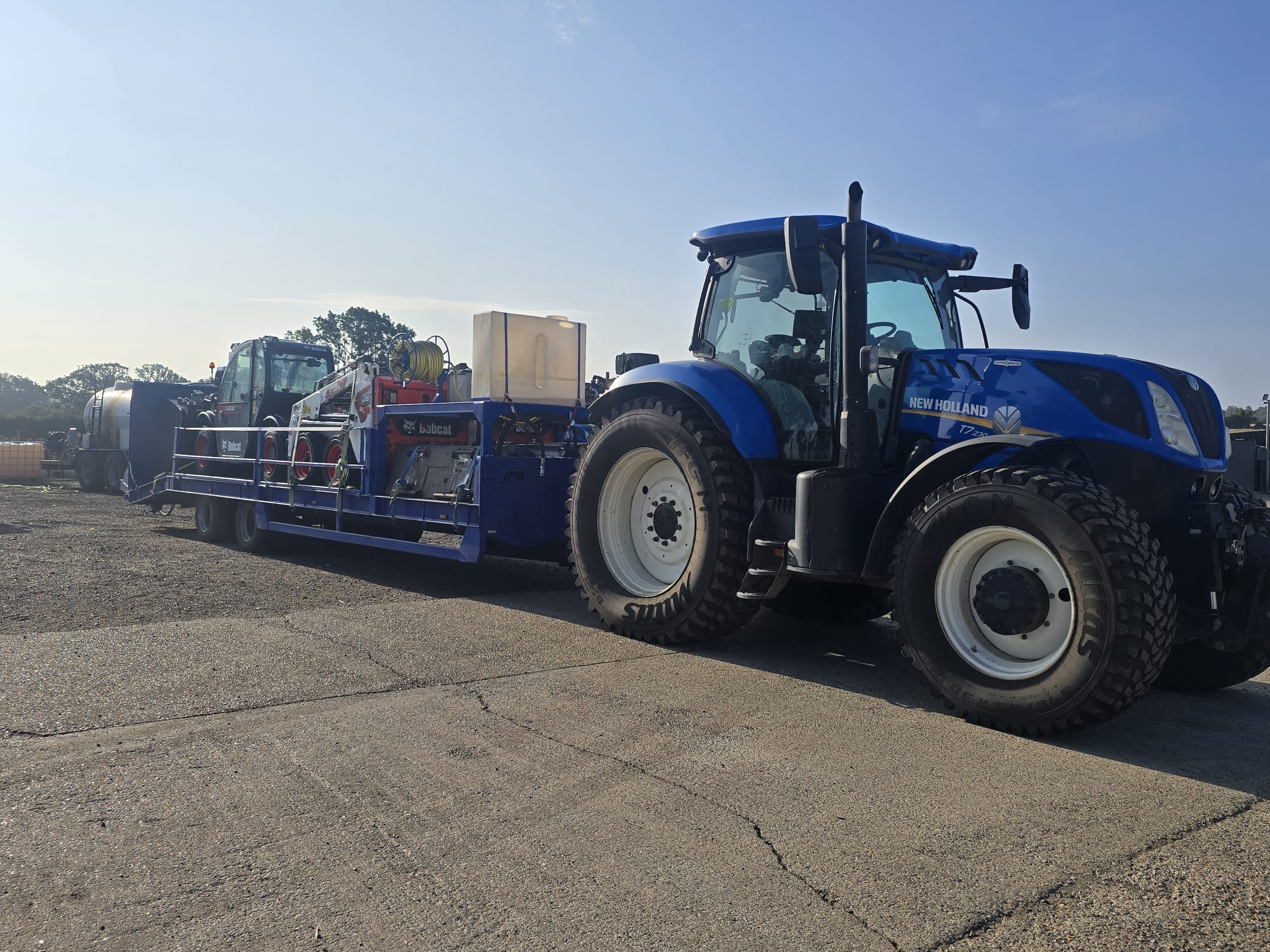 New Holland T7.230 tractor with a low-loader trailer carrying Bobcat machines